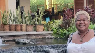  A woman stands before a fountain with a waterfall, surrounded by lush topical plants in the background