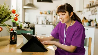 A woman in purple scrubs focused on her laptop, engrossed in her work