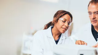 A man and woman in lab coats and safety glasses repairing a medical device