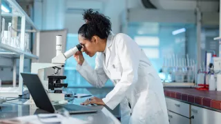 A female scientist in a lab coat examining a specimen under a microscope