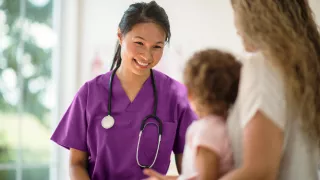 A caring nurse in purple scrubs having a conversation with a young patient