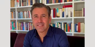 A man in a blue shirt sitting in front of a bookcase