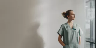 A female healthcare worker in scrubs standing by a window.