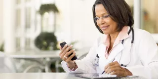 A doctor in a white coat using her cell phone