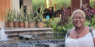  A woman stands before a fountain with a waterfall, surrounded by lush topical plants in the background
