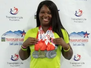 A woman proudly displaying her medals in front of a wall.