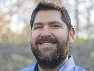  A smiling man with a beard wearing a blue shirt.