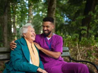 A nurse and elderly woman smiling on outdoor bench