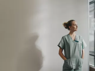 A female healthcare worker in scrubs standing by a window.
