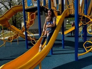  A woman and child joyfully sliding down a playground slide, enjoying a playful moment together.