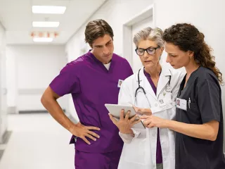 Three healthcare professionals in a hallway, attentively examining a tablet