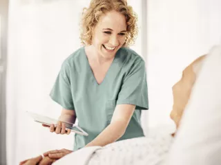 A healthcare professional at the bedside holds a tablet, providing medical care to a patient