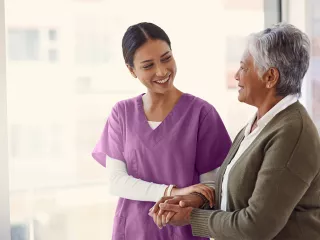 Healthcare professional and woman supporting each other in hallway with bright window in background