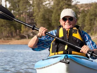 Man in sunglasses, a cap and a life jacket, kayaking on a lake