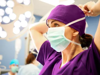 Female surgeon secures her face mask in an operating room.