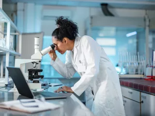 A female scientist in a lab coat examining a specimen under a microscope